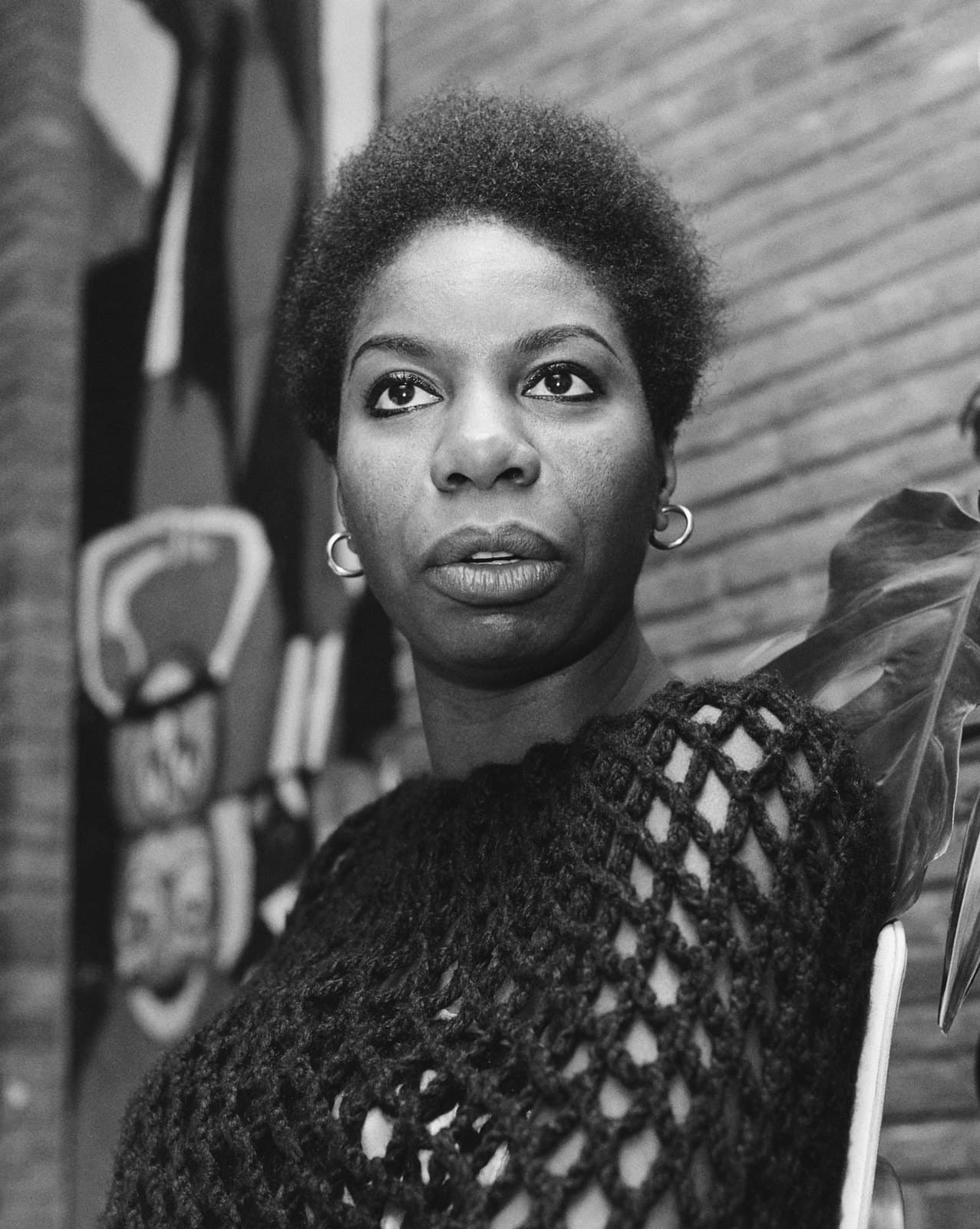 Nina Simone in a 1965 black-and-white portrait, looking directly toward the camera with her hair swept upward.