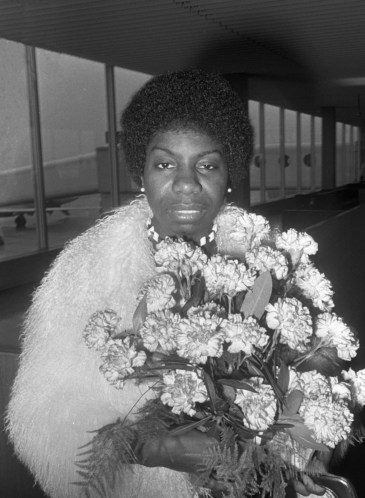 Nina Simone looking toward the camera at Schiphol Airport in 1969 while holding a large bouquet of flowers