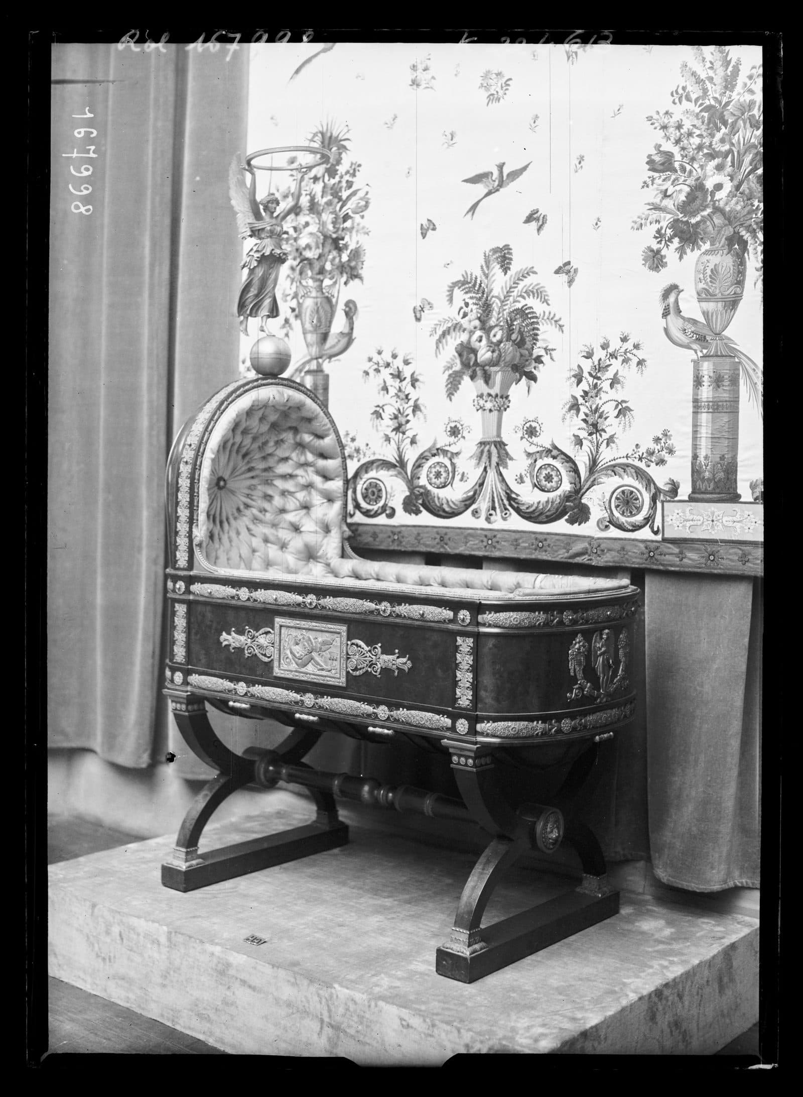 Empire-style cradle of the Roi de Rome on a velvet platform before a floral hanging, photographed at a 1932 exhibition