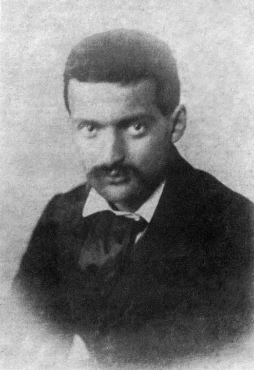 Paul Cézanne around age twenty-two, seated, with dark hair and a short beard, in a dark coat