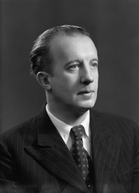 Paul Éluard in a pinstriped suit, in a formal studio portrait against a dark background.