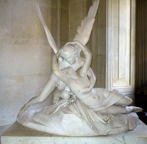 White marble sculpture of winged Cupid holding the waking Psyche, her arms raised to his head, on a rocky base