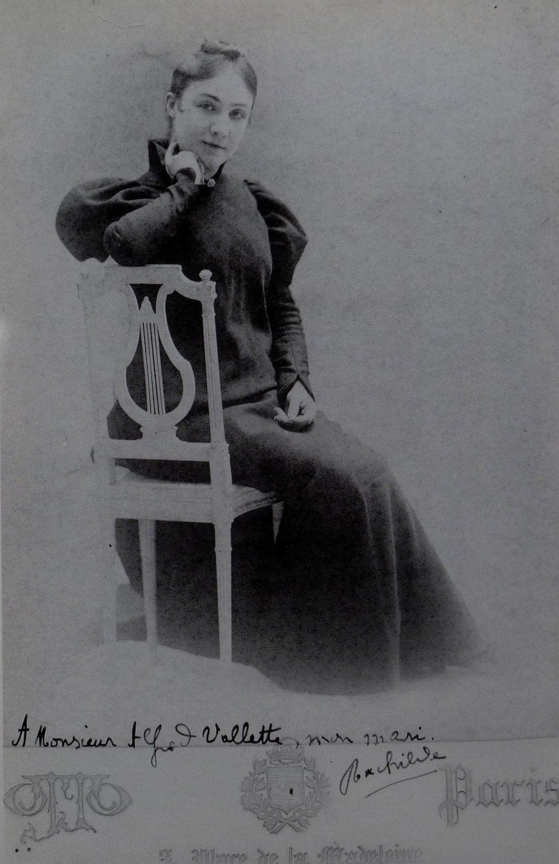 Rachilde as a young woman, seated sideways on a lyre-backed chair in a dark high-necked dress with full leg-of-mutton sleeves, chin resting on one hand. The mount is inscribed in ink and carries the Otto studio imprint.