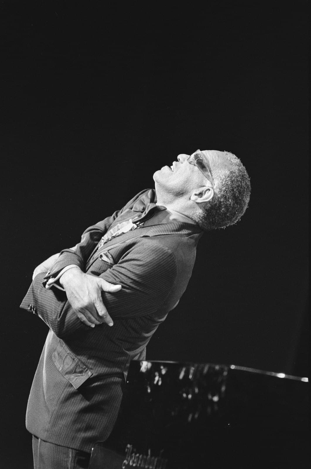 Ray Charles seated at the piano during the 1983 North Sea Jazz Festival, singing into a microphone in dark glasses.