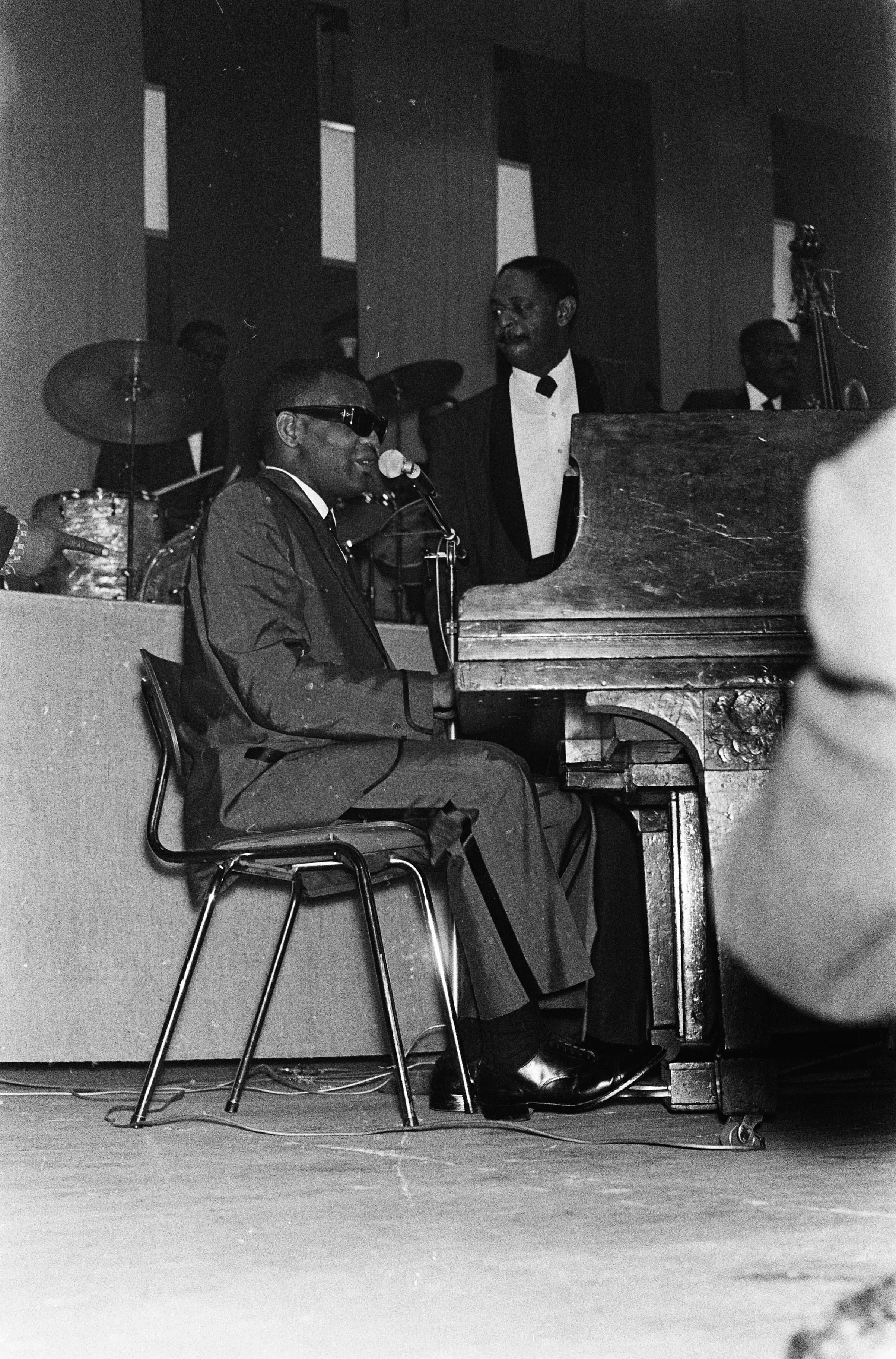 Ray Charles at a piano on stage, head tilted back, singing into a microphone during a night concert.