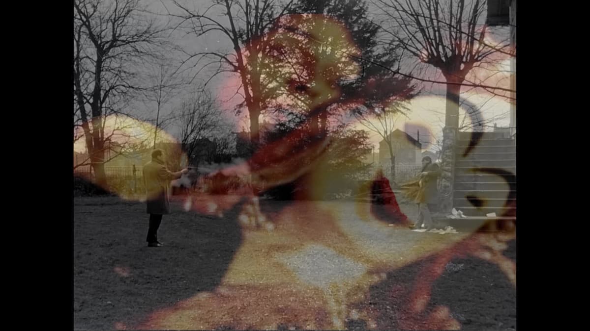 Film frame: a black-and-white park scene with bare trees, overlaid with translucent red and yellow painted shapes