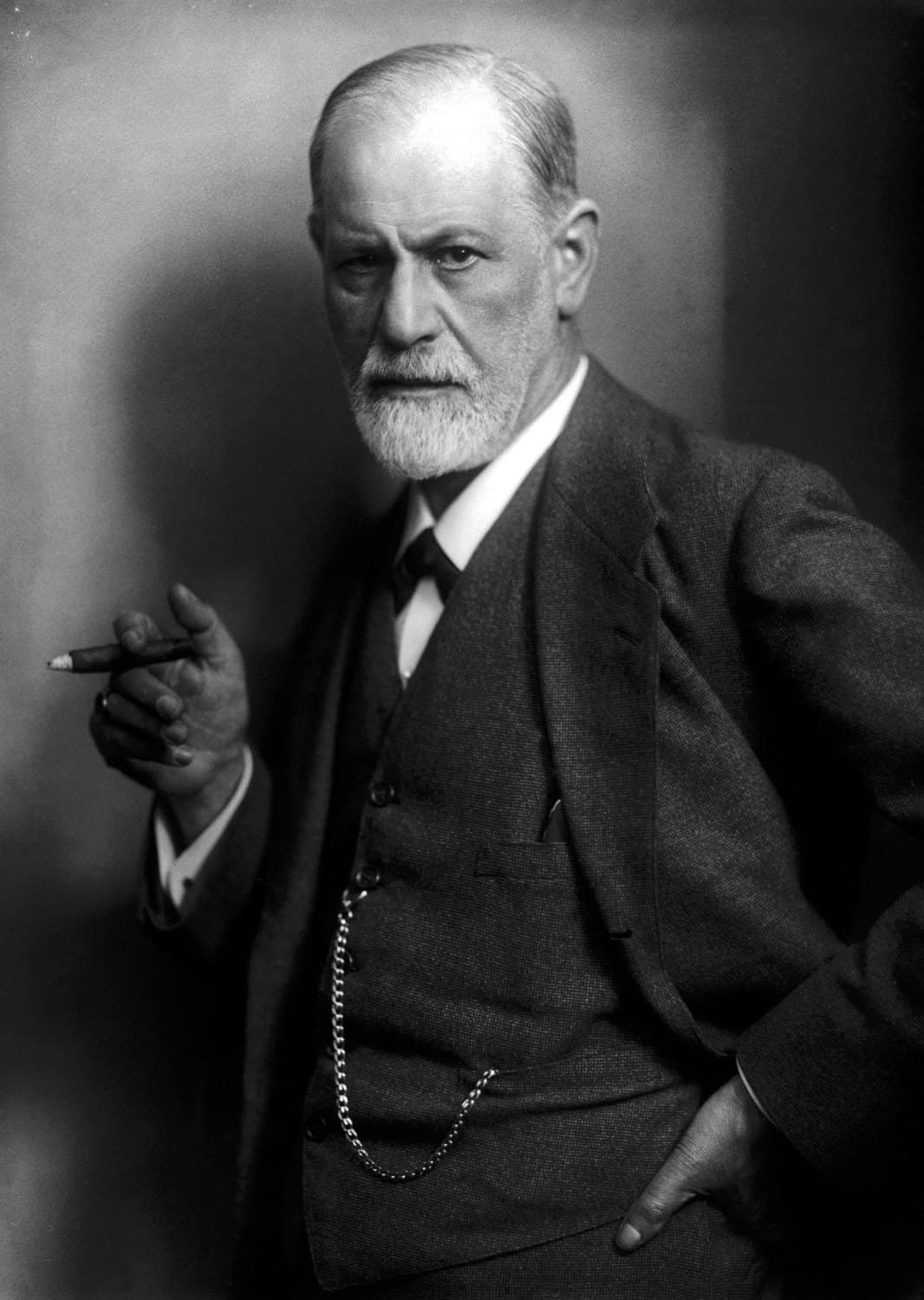 Sigmund Freud in a three-piece suit with a watch chain, holding a cigar and looking directly at the camera.