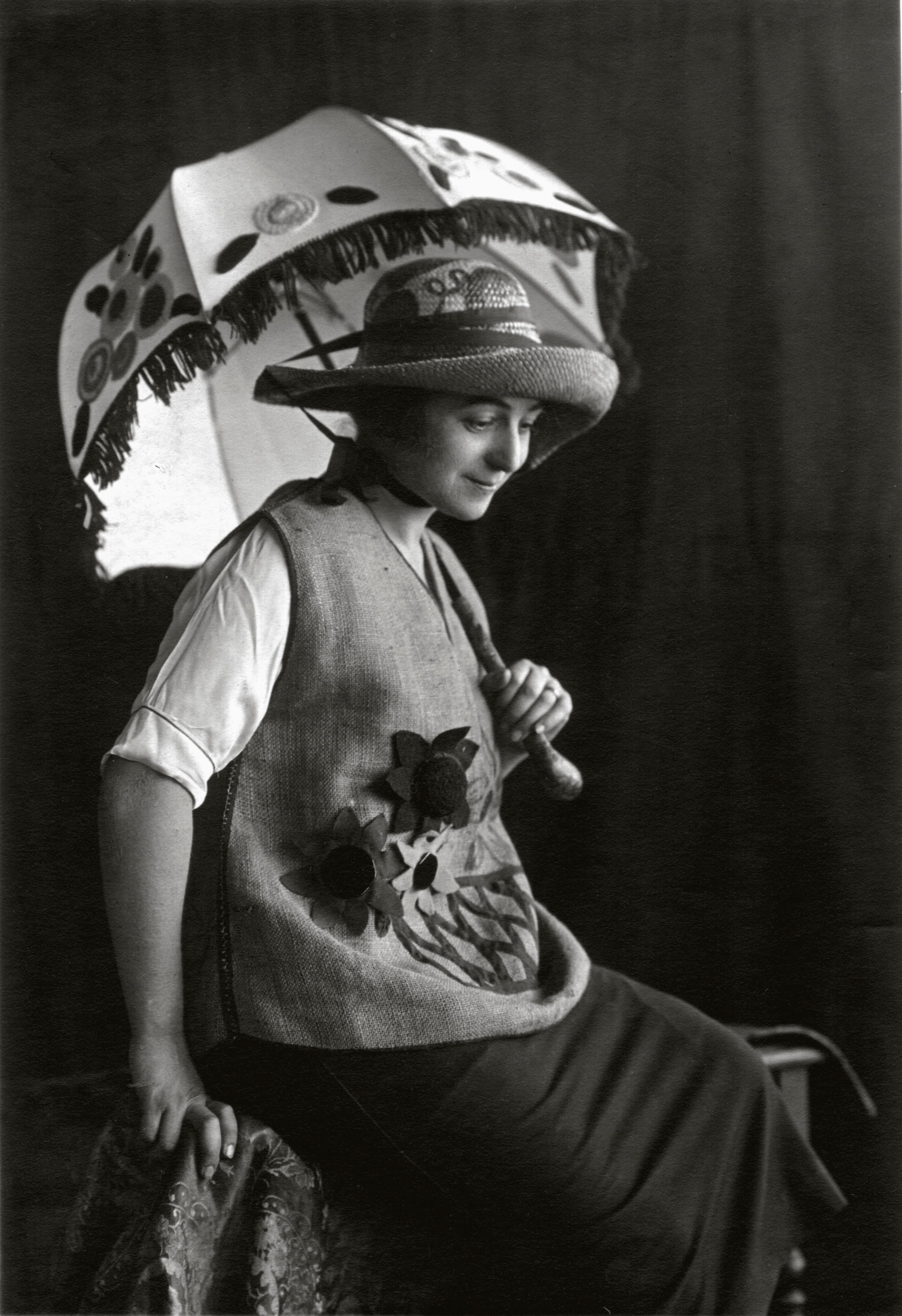 Sonia Delaunay standing in a patterned coat and turban of her own design, one hand on a draped table