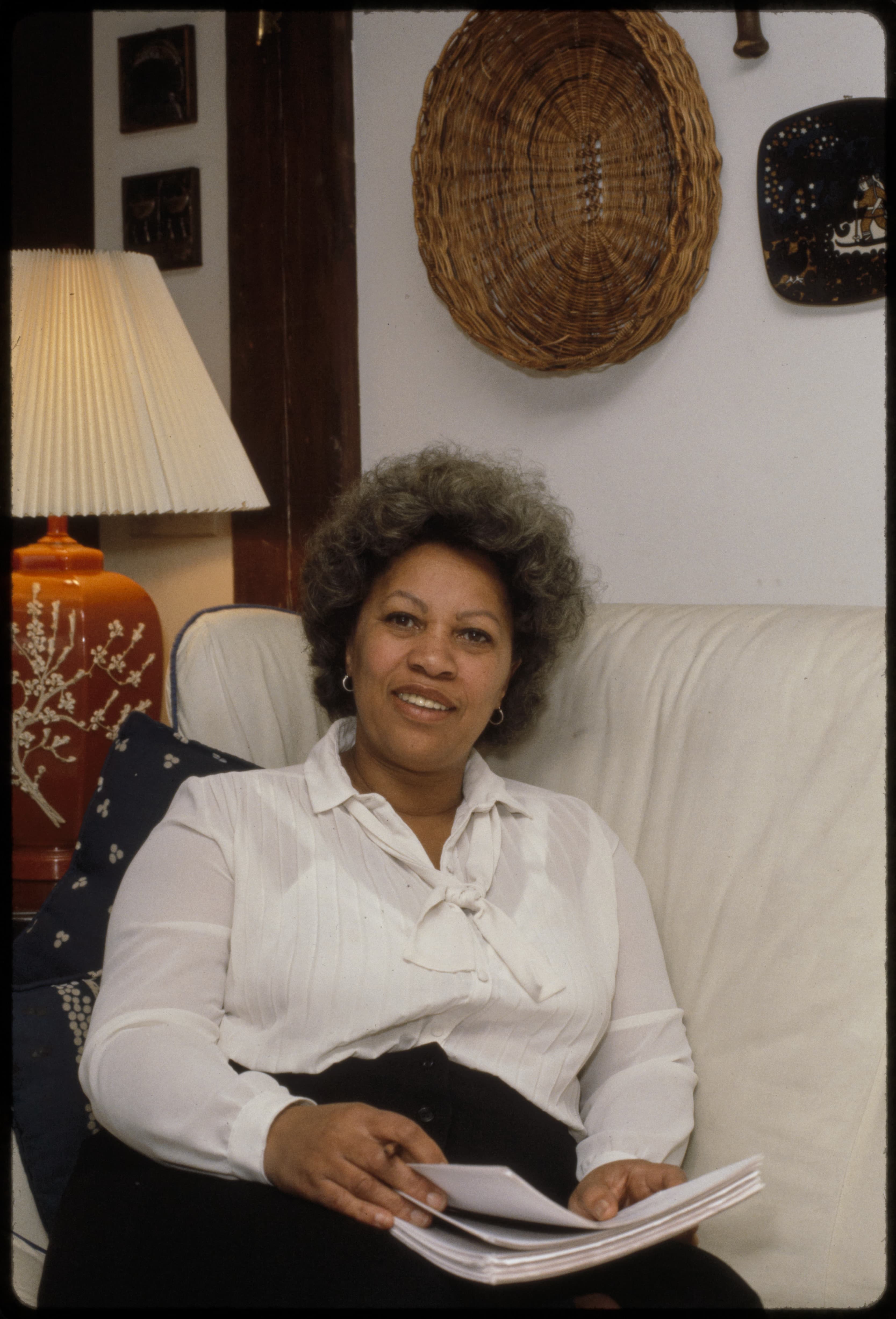 Toni Morrison seated at home beside a window, looking towards the camera.