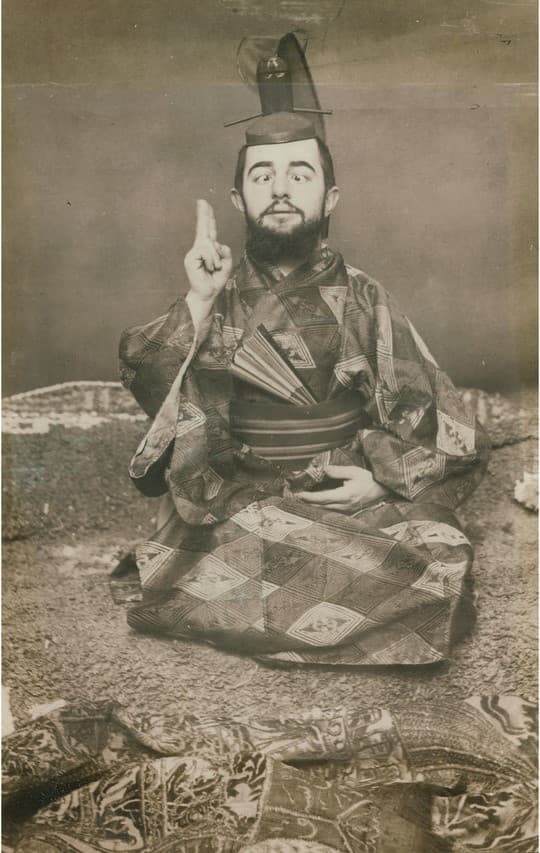 Toulouse-Lautrec seated cross-legged in a Japanese robe, holding a fan and crossing his eyes at the camera