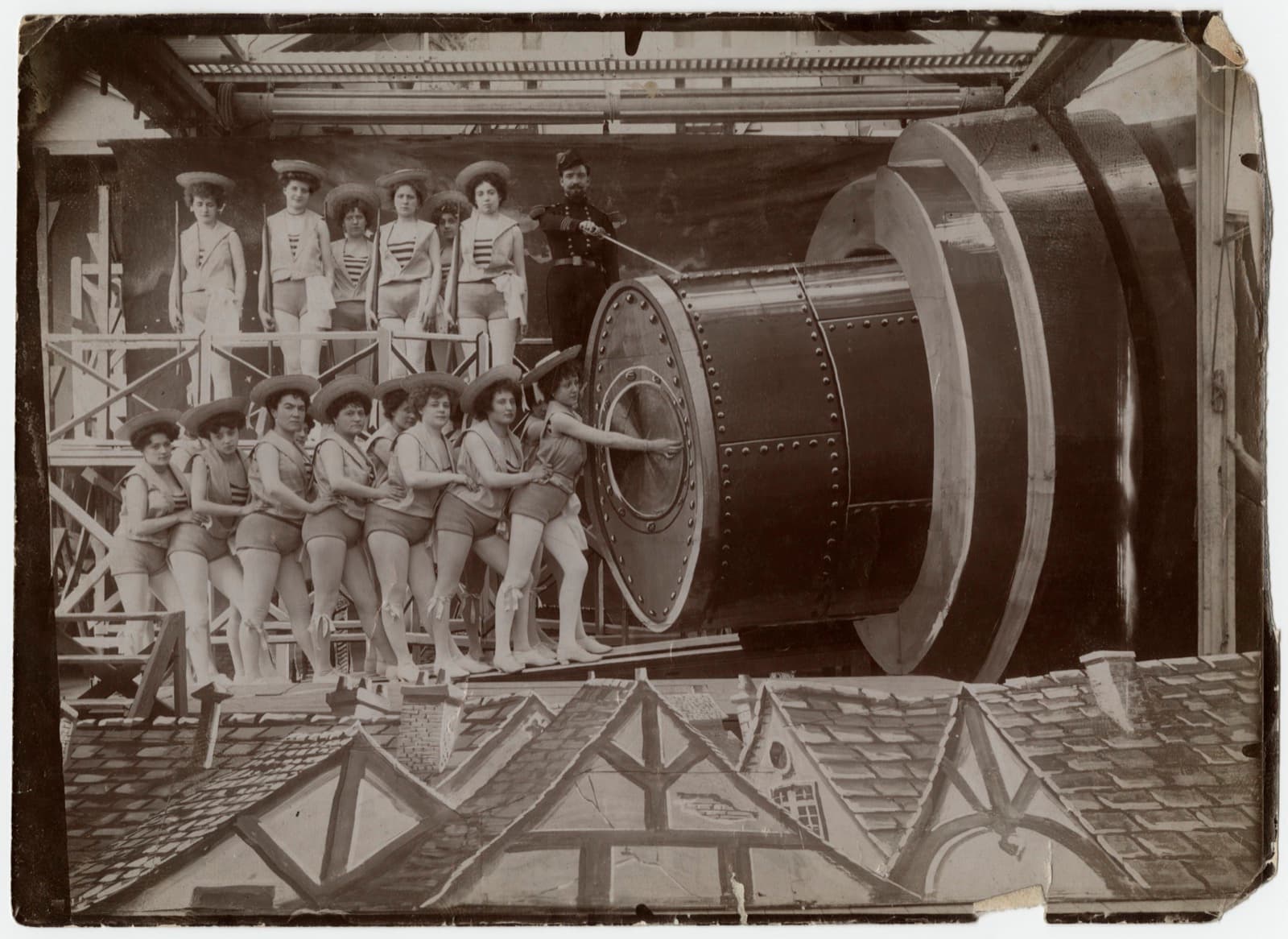 Production still from A Trip to the Moon: a chorus line in sailor suits pushes the capsule into the giant cannon's breech above painted village rooftops