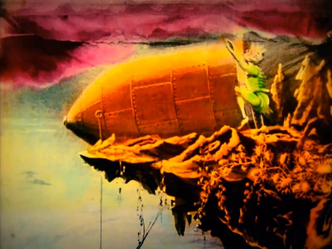 Hand-colored frame from A Trip to the Moon: a green Selenite clings to the capsule as it tips over the lunar cliff toward the sea below