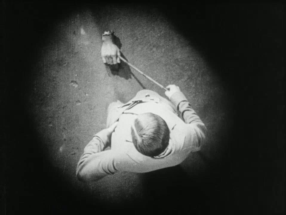 Overhead iris shot: an androgynous figure prods a severed hand on the pavement with a cane, from Un Chien Andalou