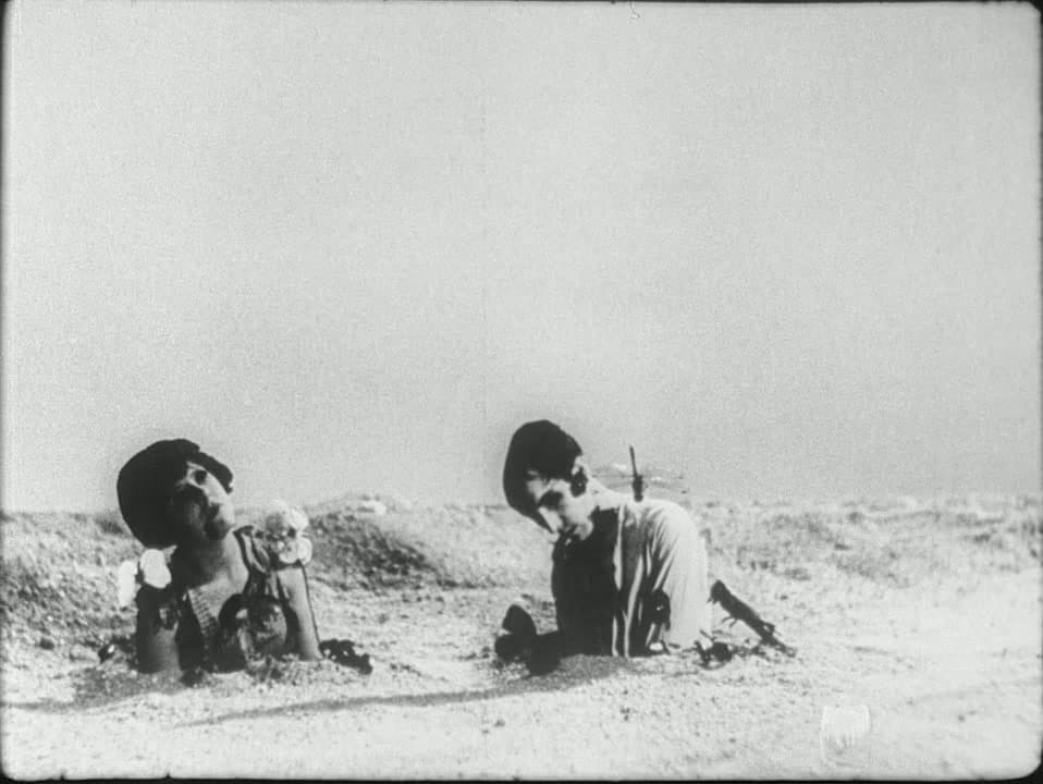 A woman and a man buried to their chests in beach sand under a blank sky — the final shot of Un Chien Andalou