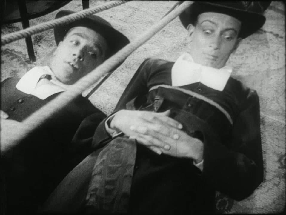 Two Marist brothers in clerical collars lie on the floor tangled in ropes, looking up, in Un Chien Andalou