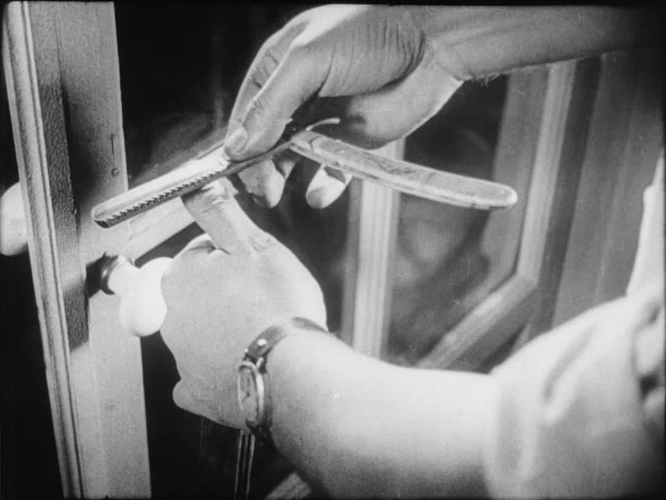 Hands strop a straight razor against a window frame at night, a wristwatch on one wrist, from the prologue of Un Chien Andalou