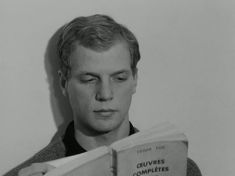 A young blond man reading from a book whose cover reads Œuvres complètes, Edgar Poe