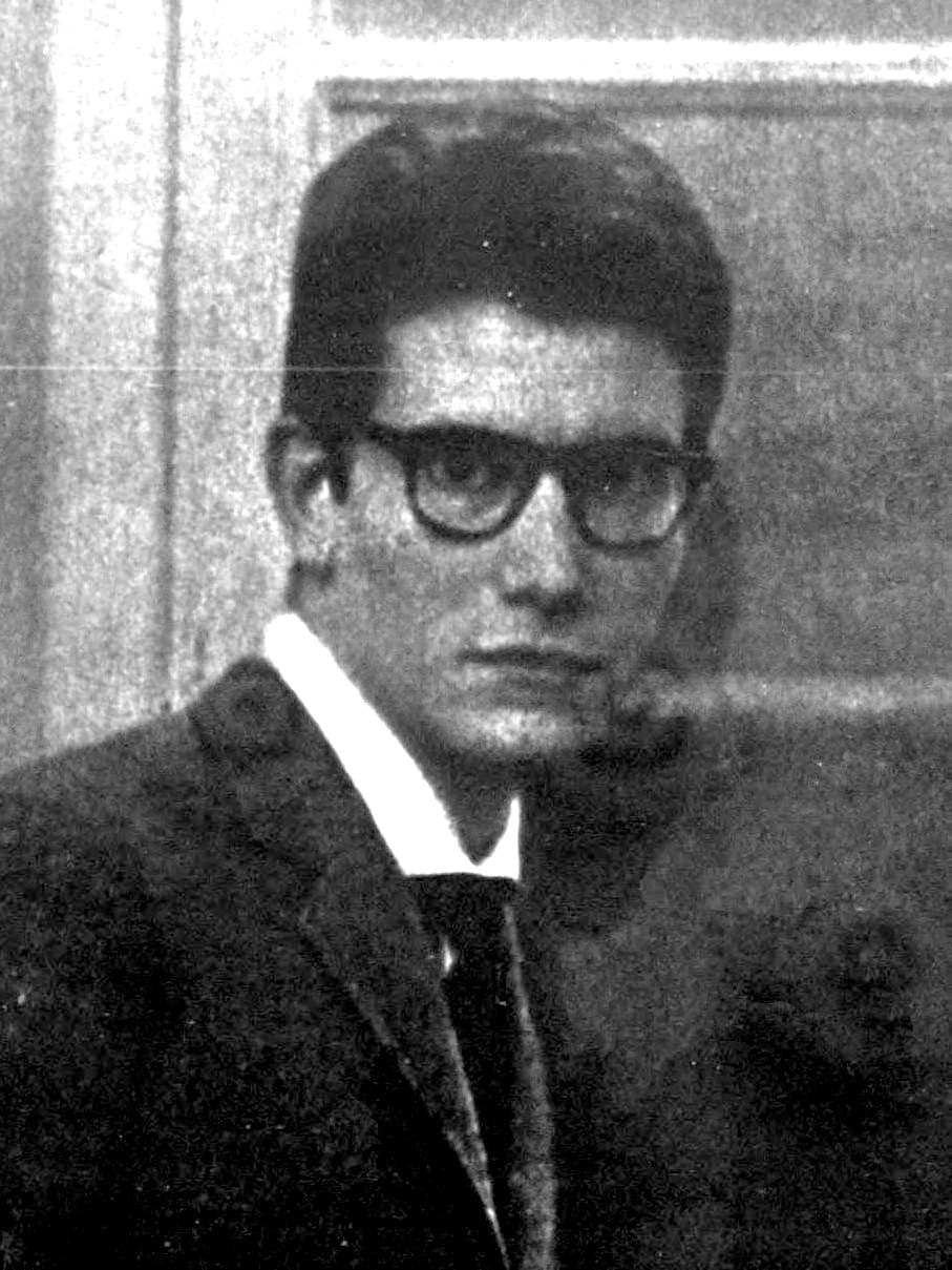 Yves Saint Laurent, wearing dark-framed glasses, seated at a worktable in his Paris studio in December 1961