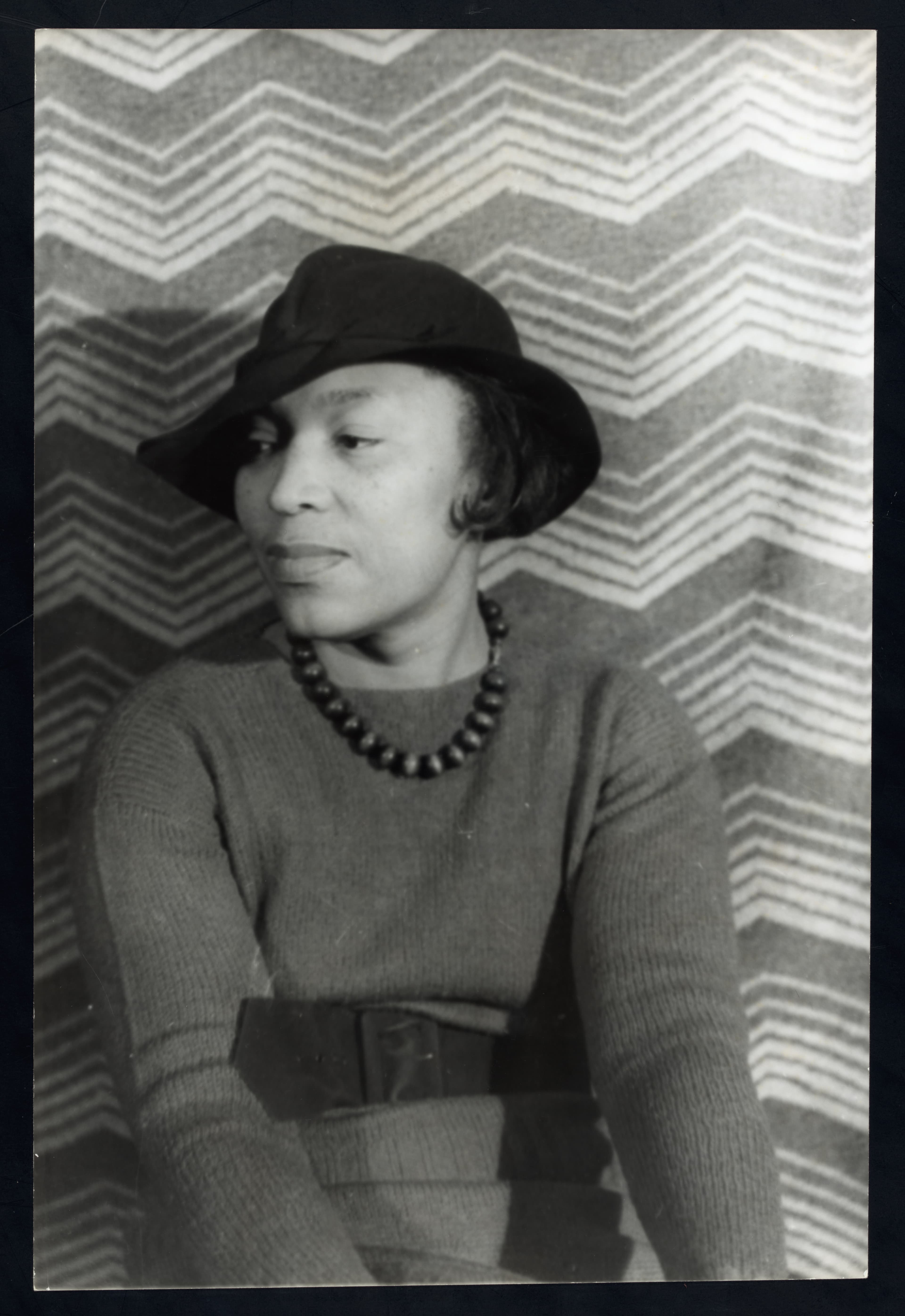 Zora Neale Hurston photographed in 1938, wearing a hat and a striped patterned jacket, half-length portrait facing the camera